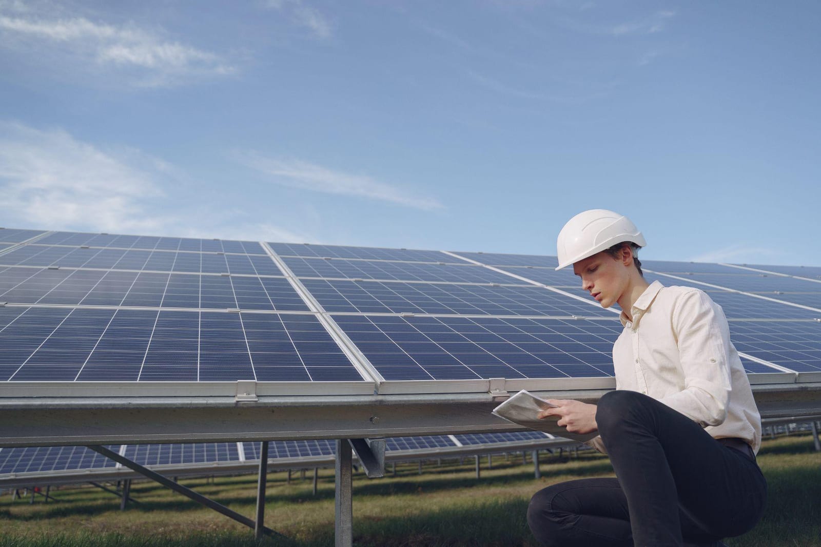 An engineer in a hard hat reviewing a tablet in front of a solar panel array
