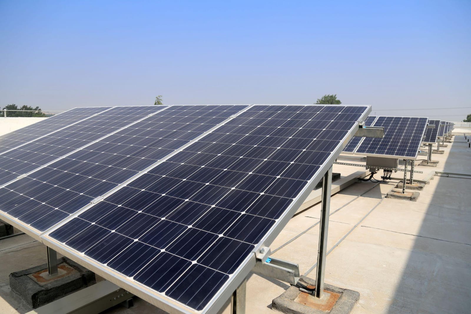 A rooftop solar array on tilt frames under a clear blue sky