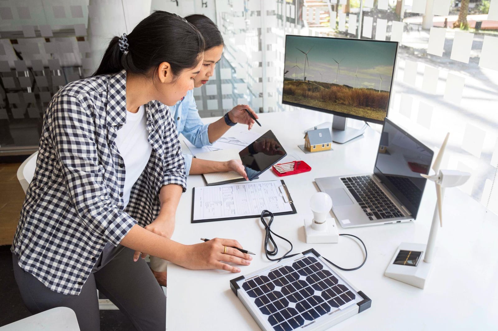 Two people reviewing solar plans at a desk with a model house and wind turbine